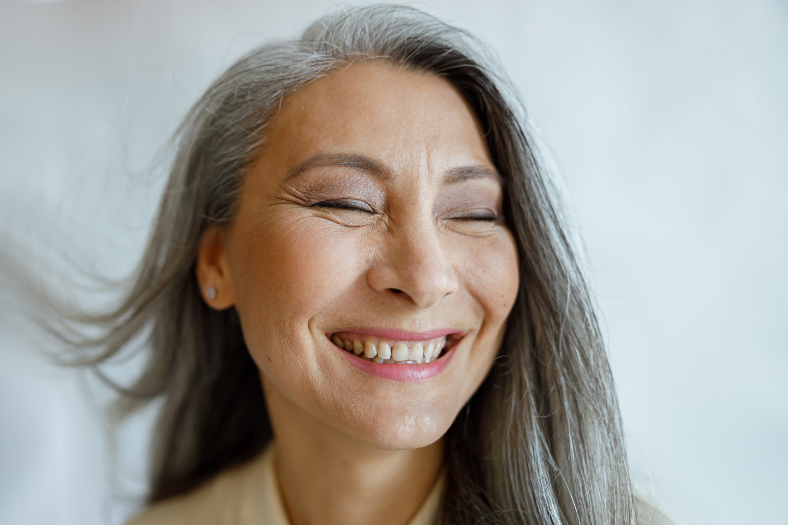 Photo of a mature Asian woman with long gray hair, smiling widely with her eyes closed.