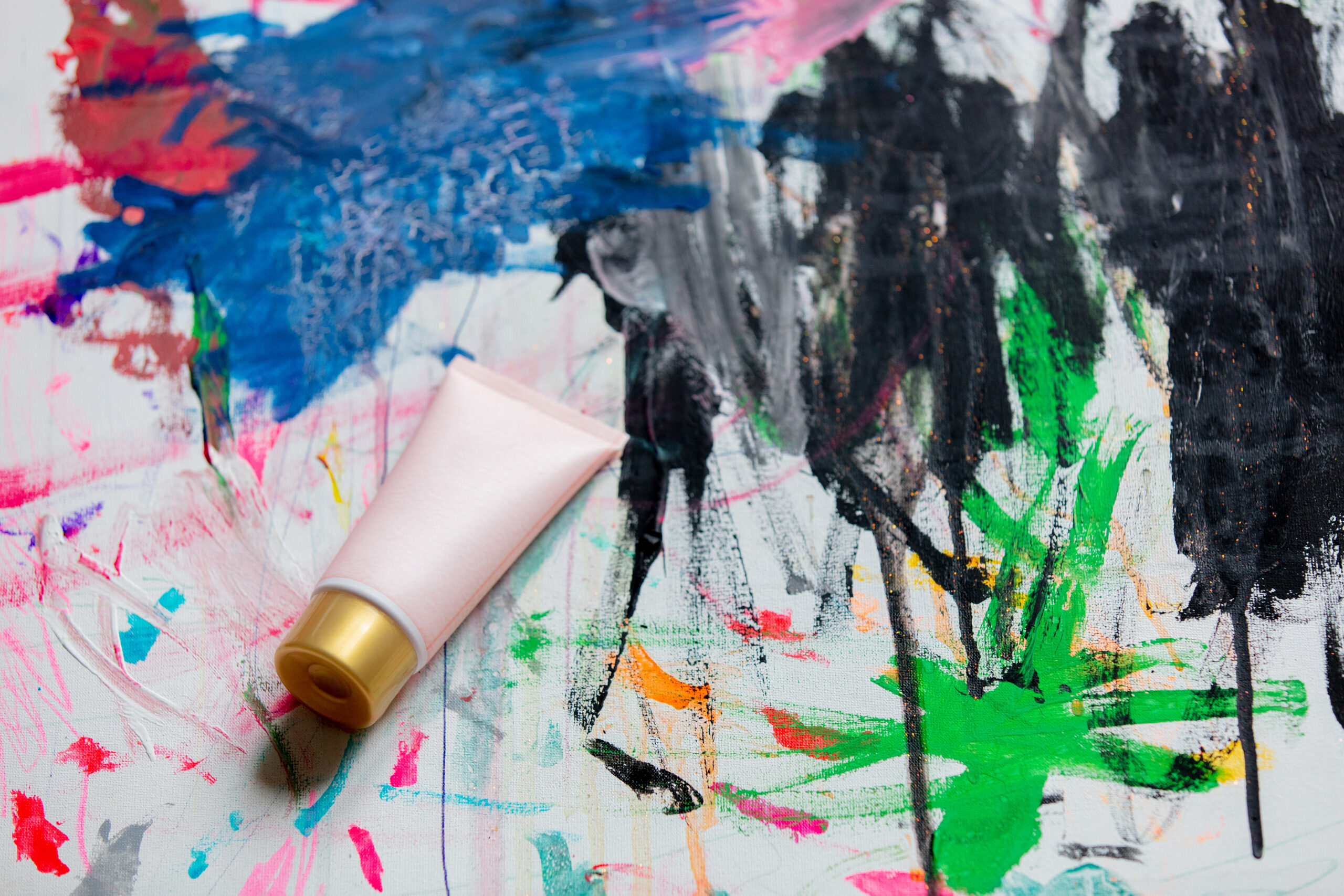 Photo of a canvas with messy and colorful paint streaks and a pink tube of paint.