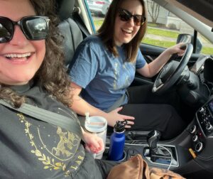Photo of Maegan and her friend Natalie, both White women with brown hair and sunglasses, sitting in the car about to embark on their binge-reading weekend.