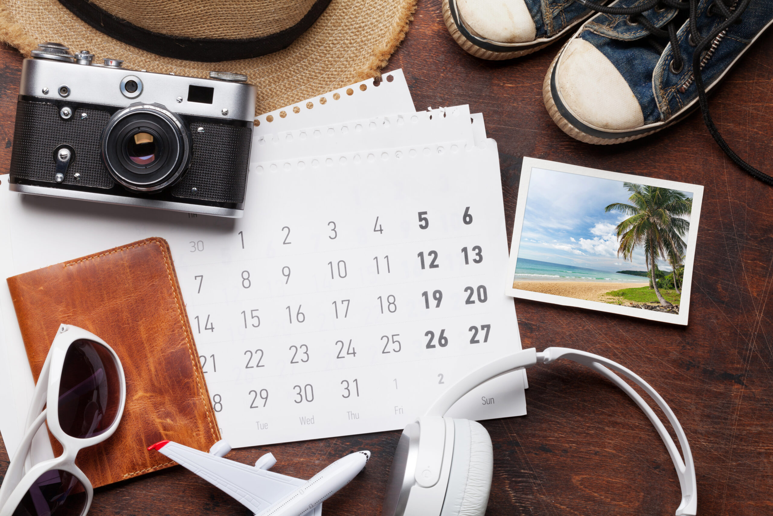 Image is a travel vacation concept with accessories, headphones, beach hat, camera, passport, airplane toy, calendar and photo.