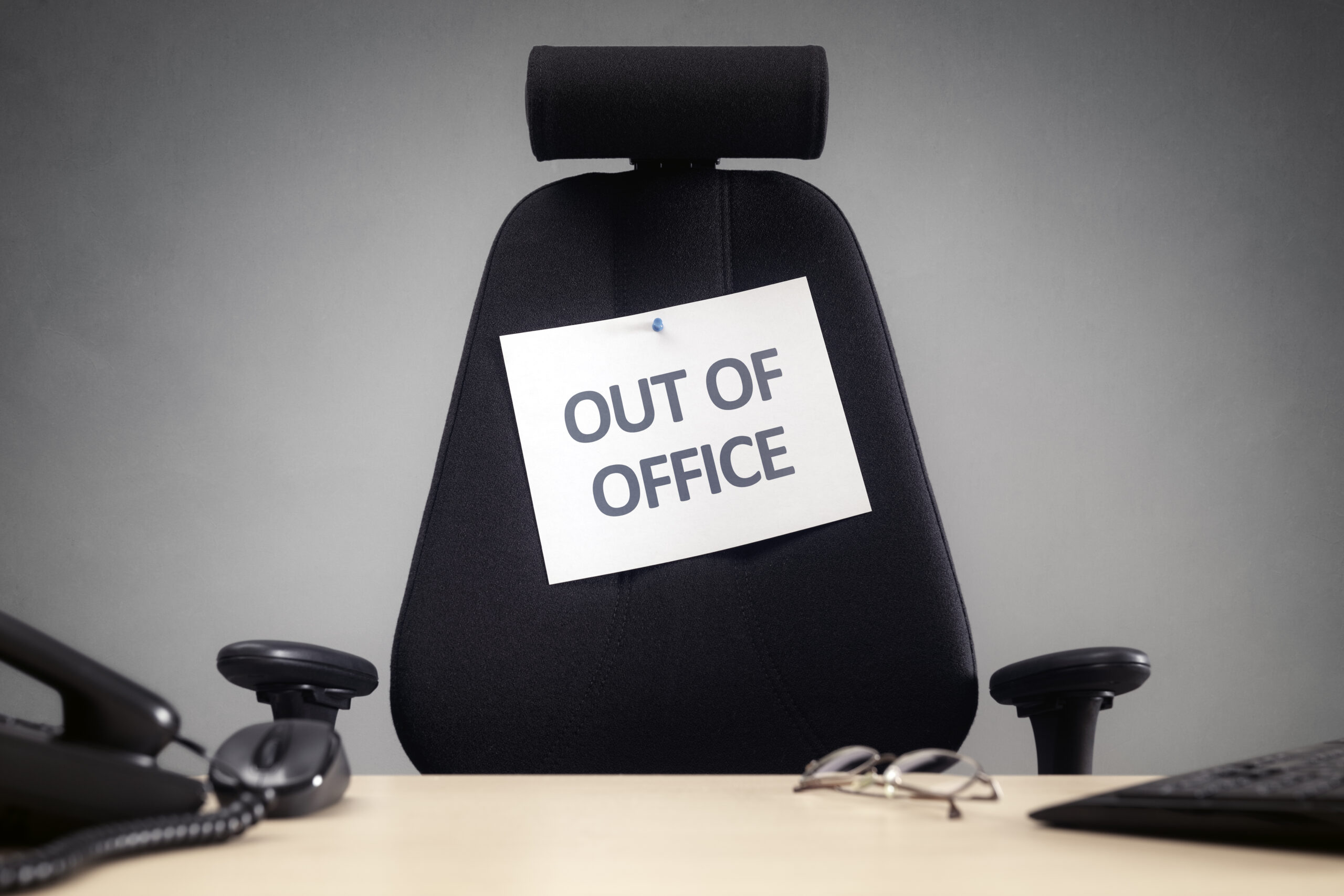 Image of an empty office chair with a sign posted on it reading, "Out of Office."