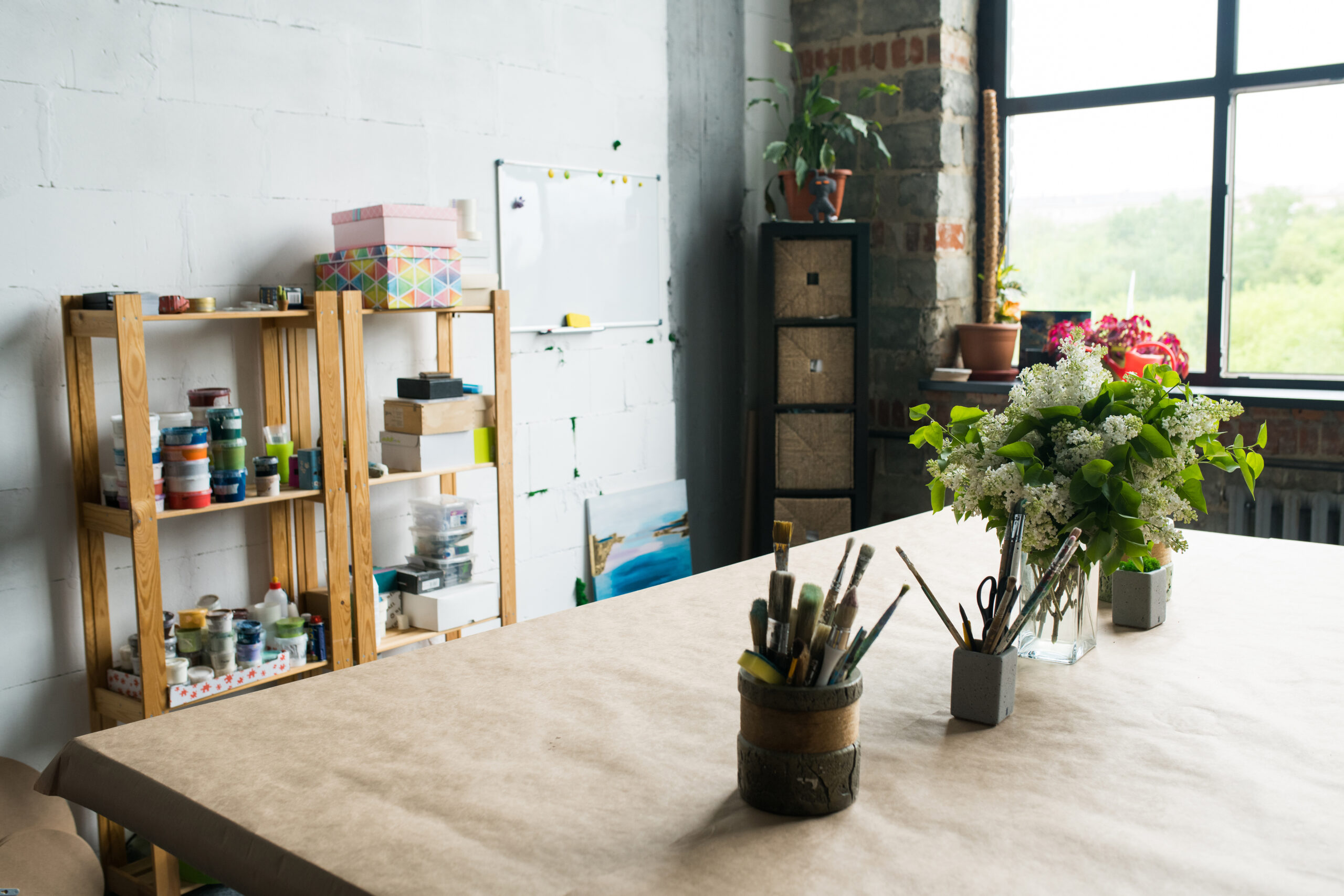 Photo of a clean and organized creative space with flowers on the table and a large window.