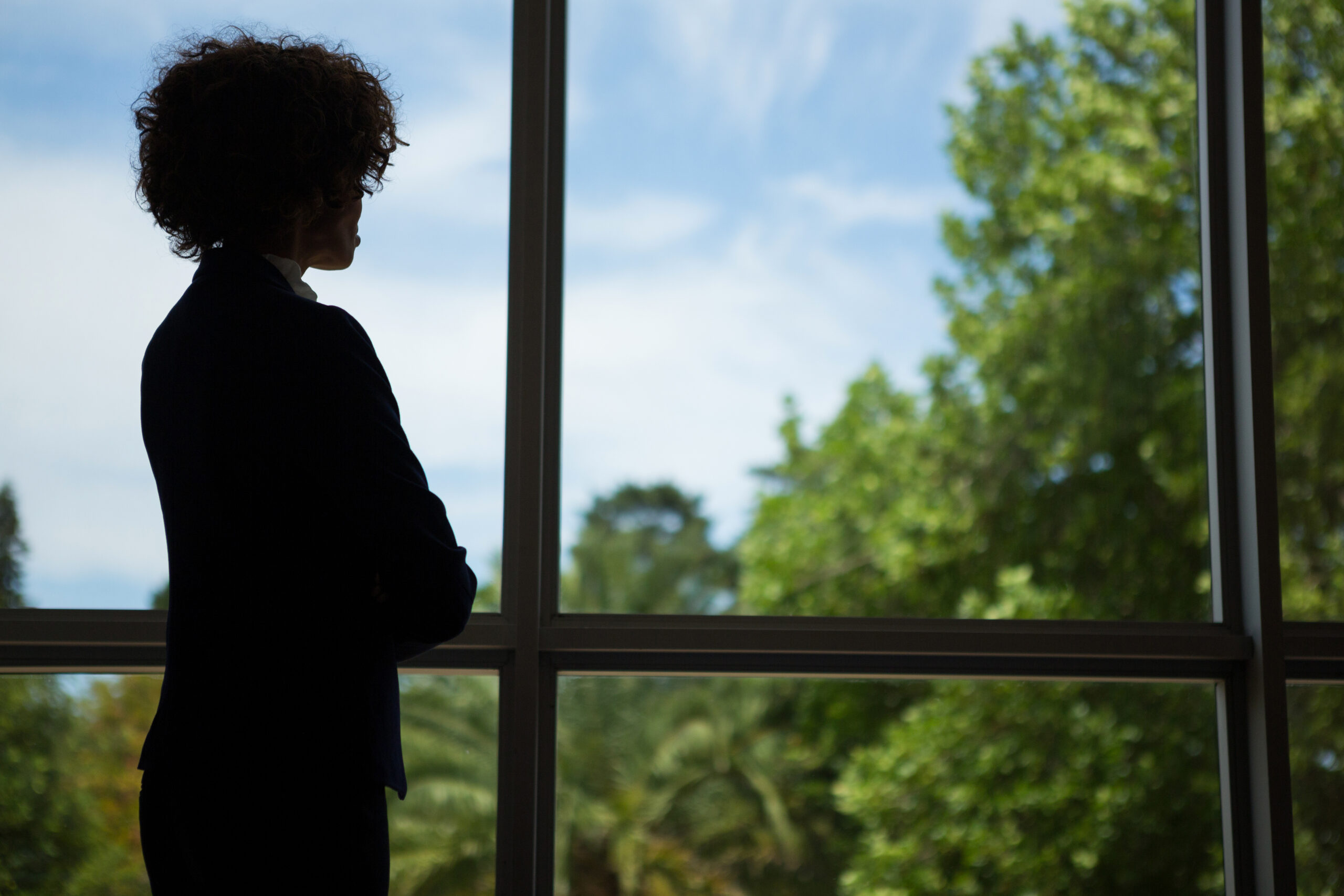 Photo of the silhouette of a woman looking out of a floor-to-ceiling window.