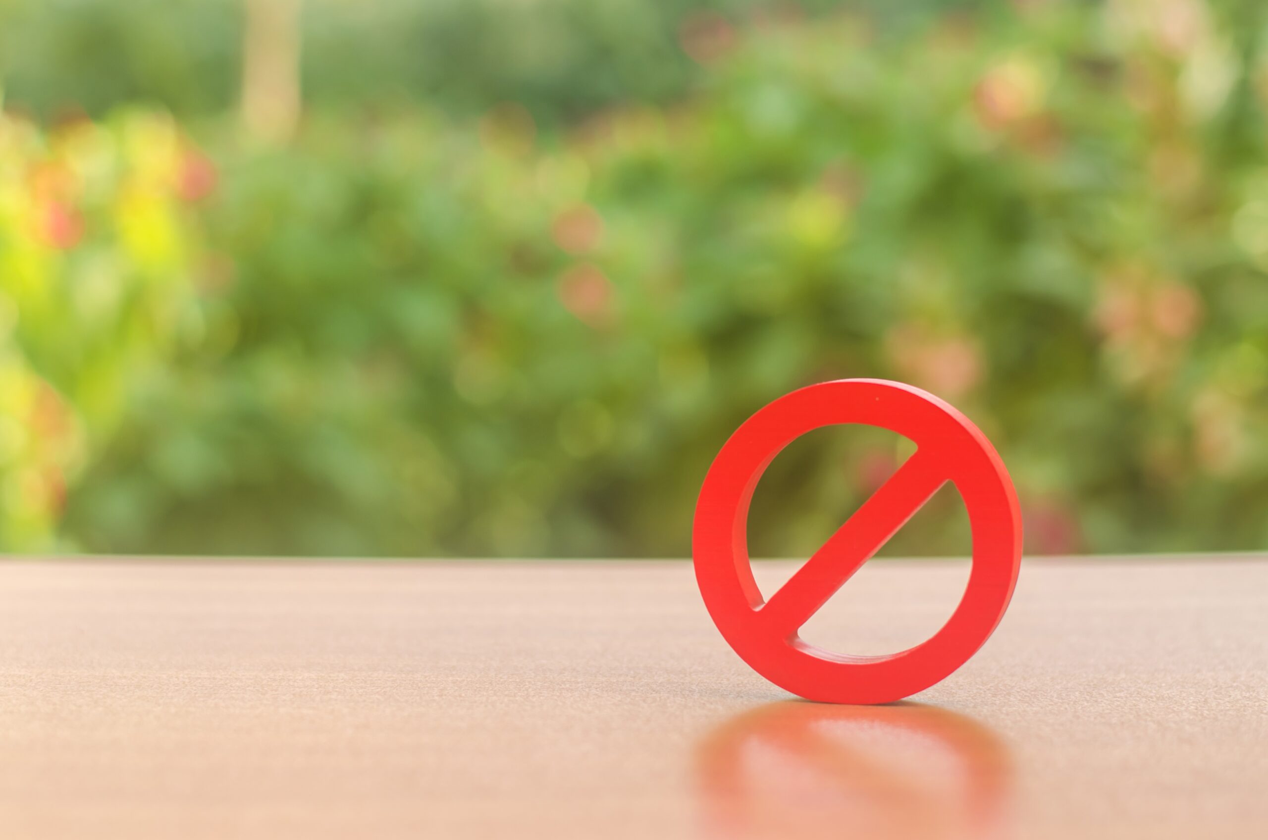 Image of a red circle with a line through it, representing "NO", with a green and brown background.
