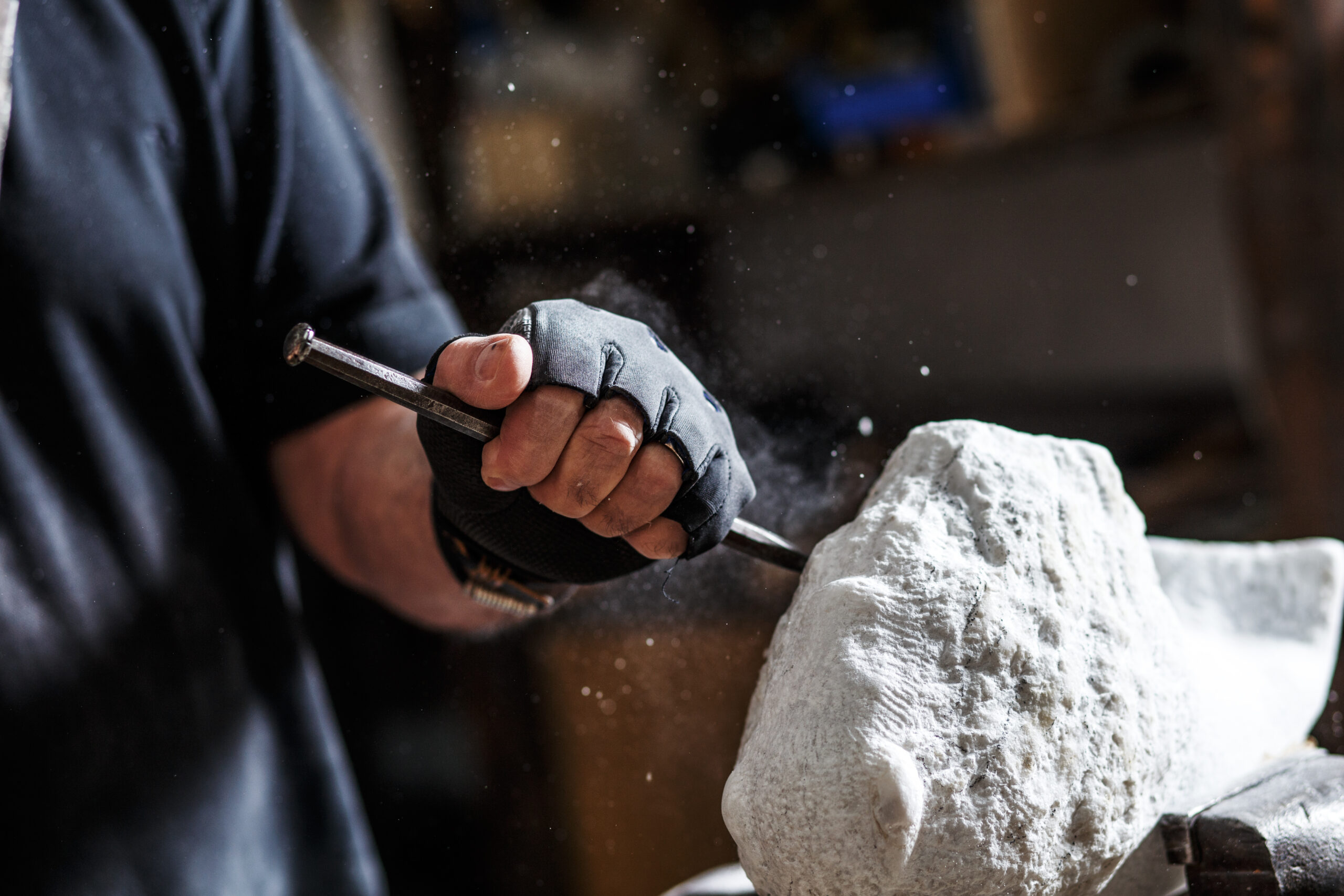 Photo of a sculptor's hands working on their marble sculpture in his workshop with hammer and chisel.