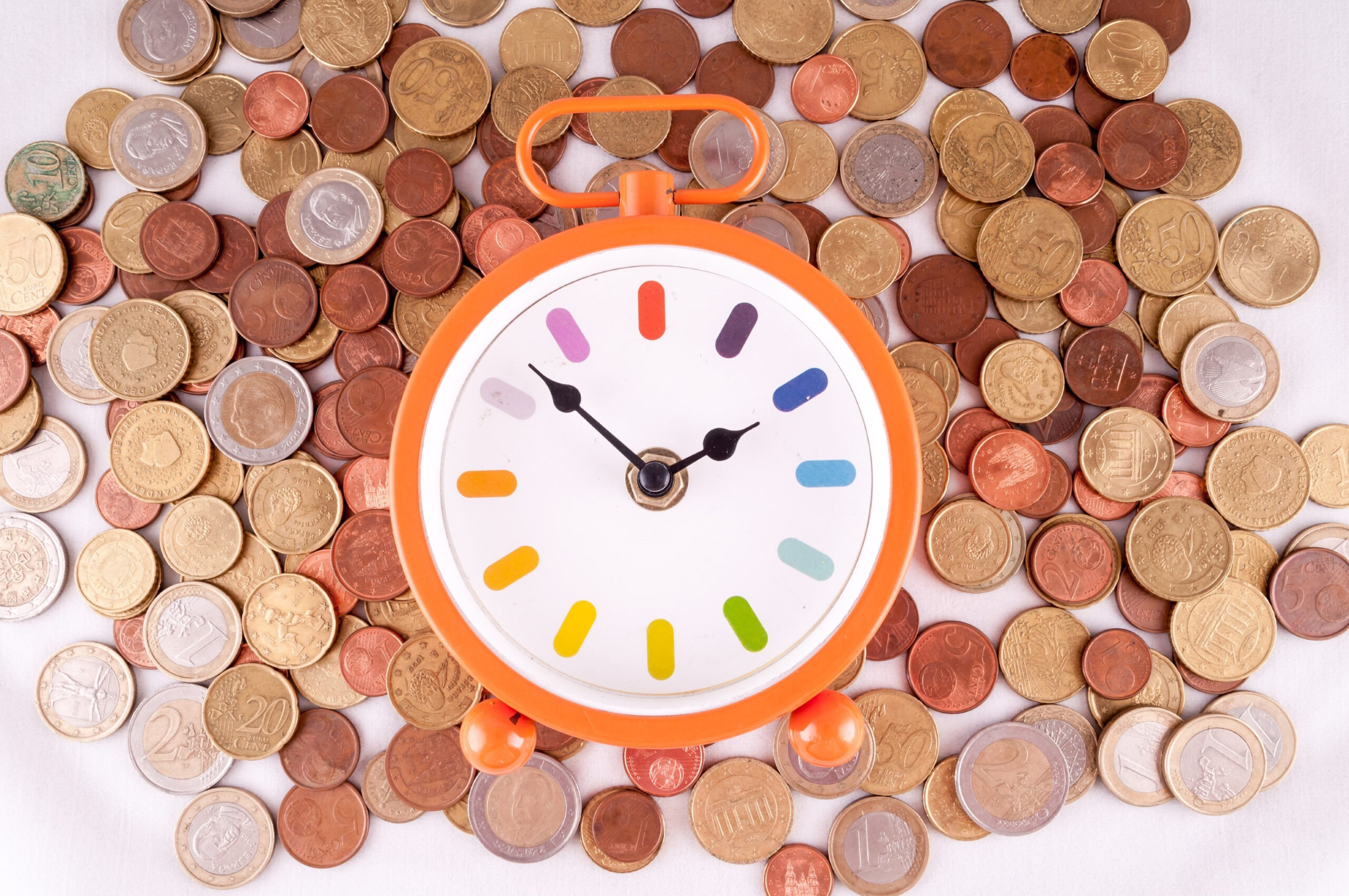 Photo of a colorful clock on top of a bunch of various types of coins.