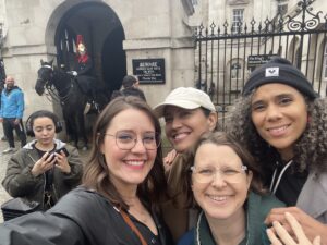 Photo of Maegan and her friends Annie, Linzy, and Tiffany posing together in front of a palace, with a guard on horseback in the background.