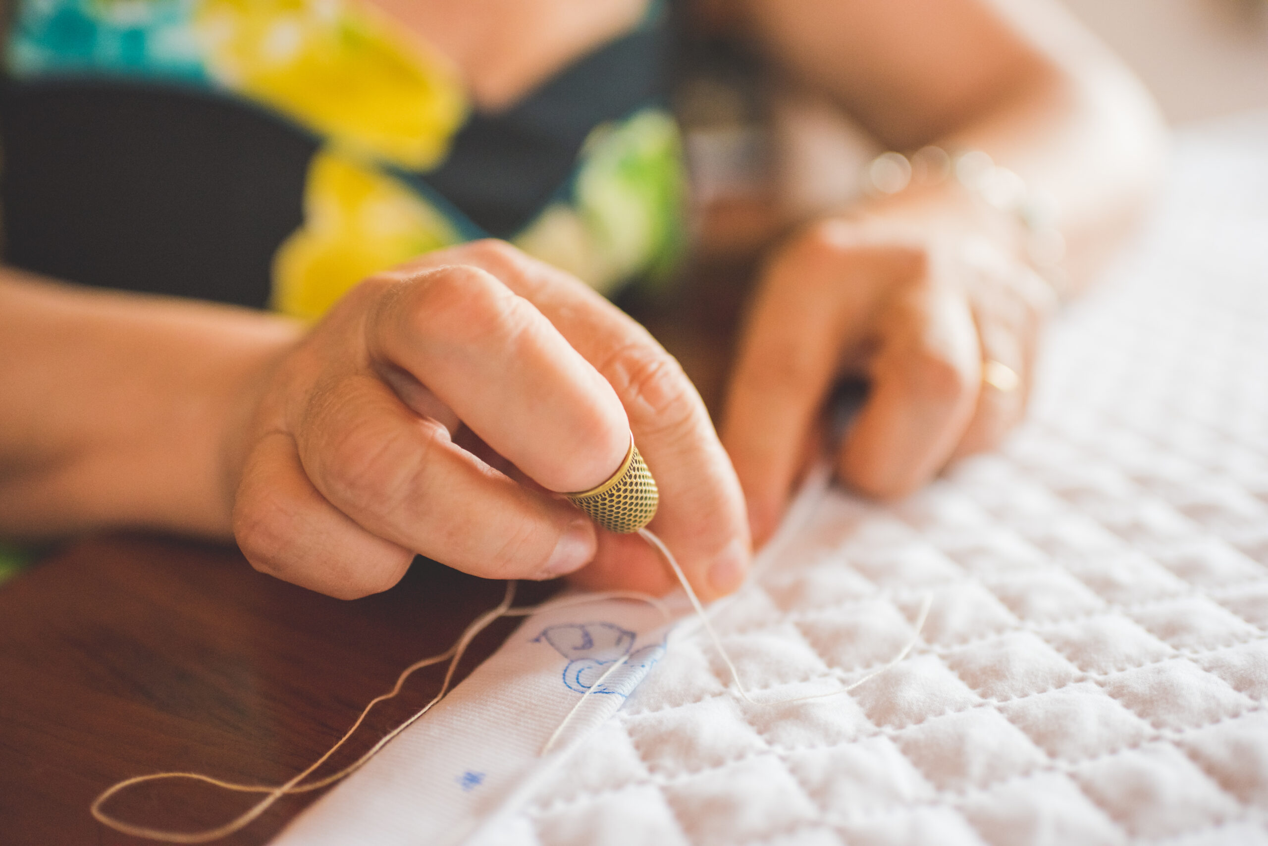 Photo is a close up of a woman's hands stitching a quilt.