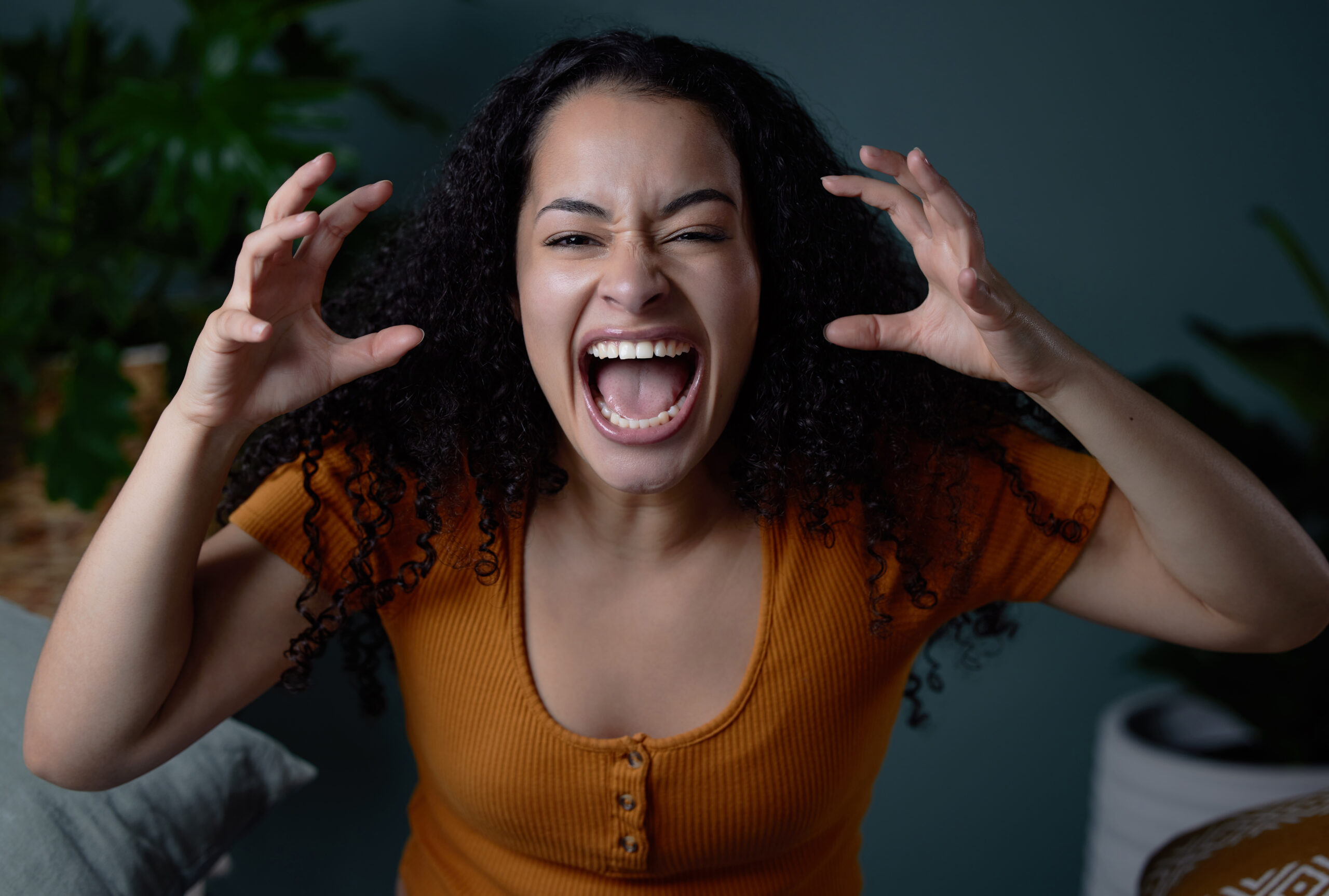 Woman with dark hair and light brown skin screaming with her hands up near her head.