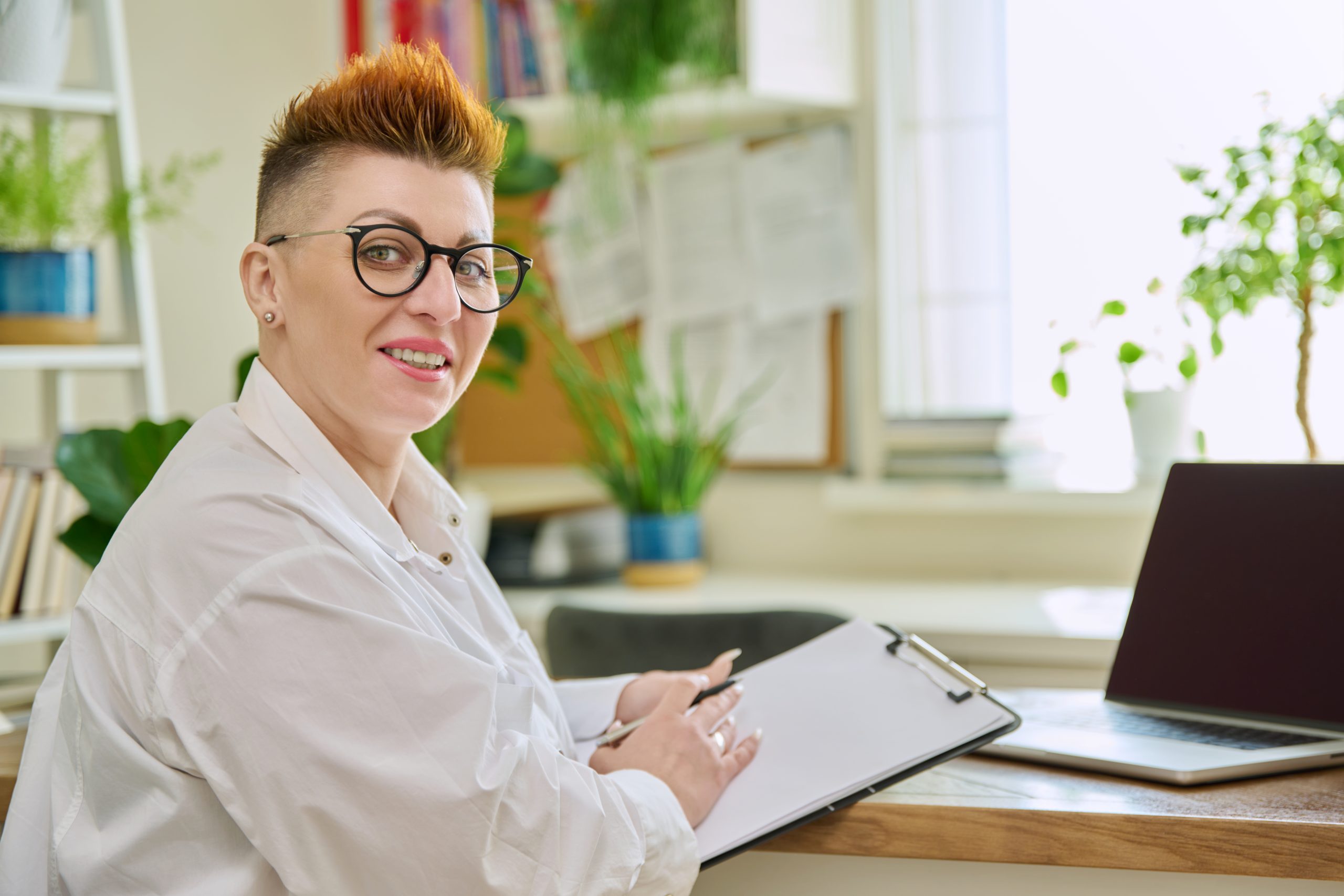 Portrait of smiling female psychotherapist with clipboard at workplace in office. Professional mental therapist counselor psychologist social worker looking at camera. Health care services, treatment