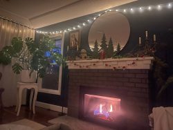 Maegan's living room, with holiday lights strung around the room, evergreen holiday decor on the mantle above the lit fireplace.